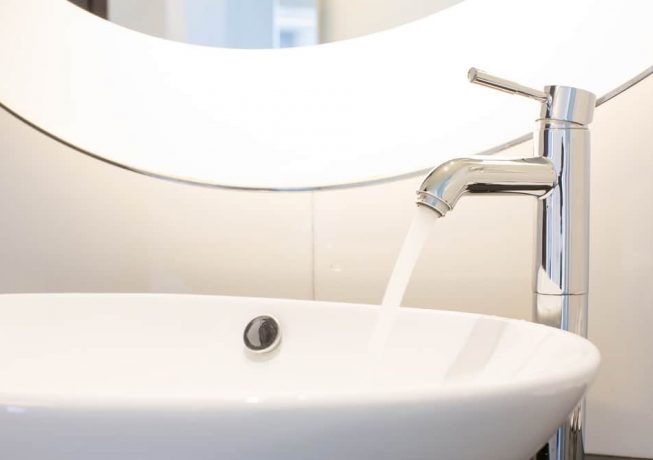 Modern bathroom faucet with round mirror — Expert Plumbers in Burleigh Heads, QLD